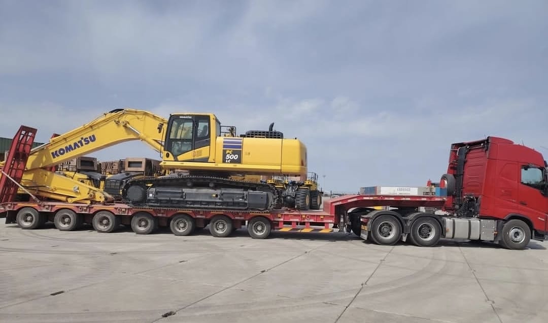 Red truck transporting yellow Komatsu excavator