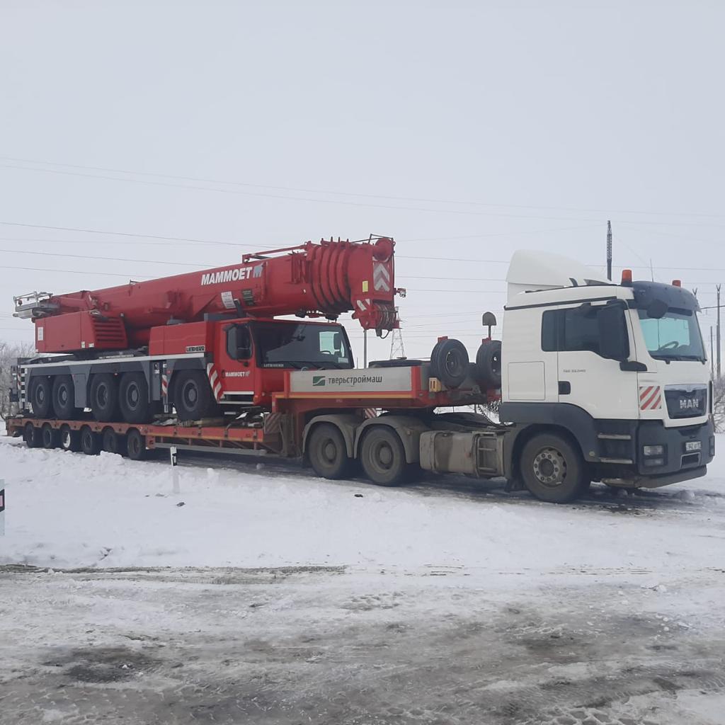 White MAN truck transporting red Mammoet mobile crane in winter