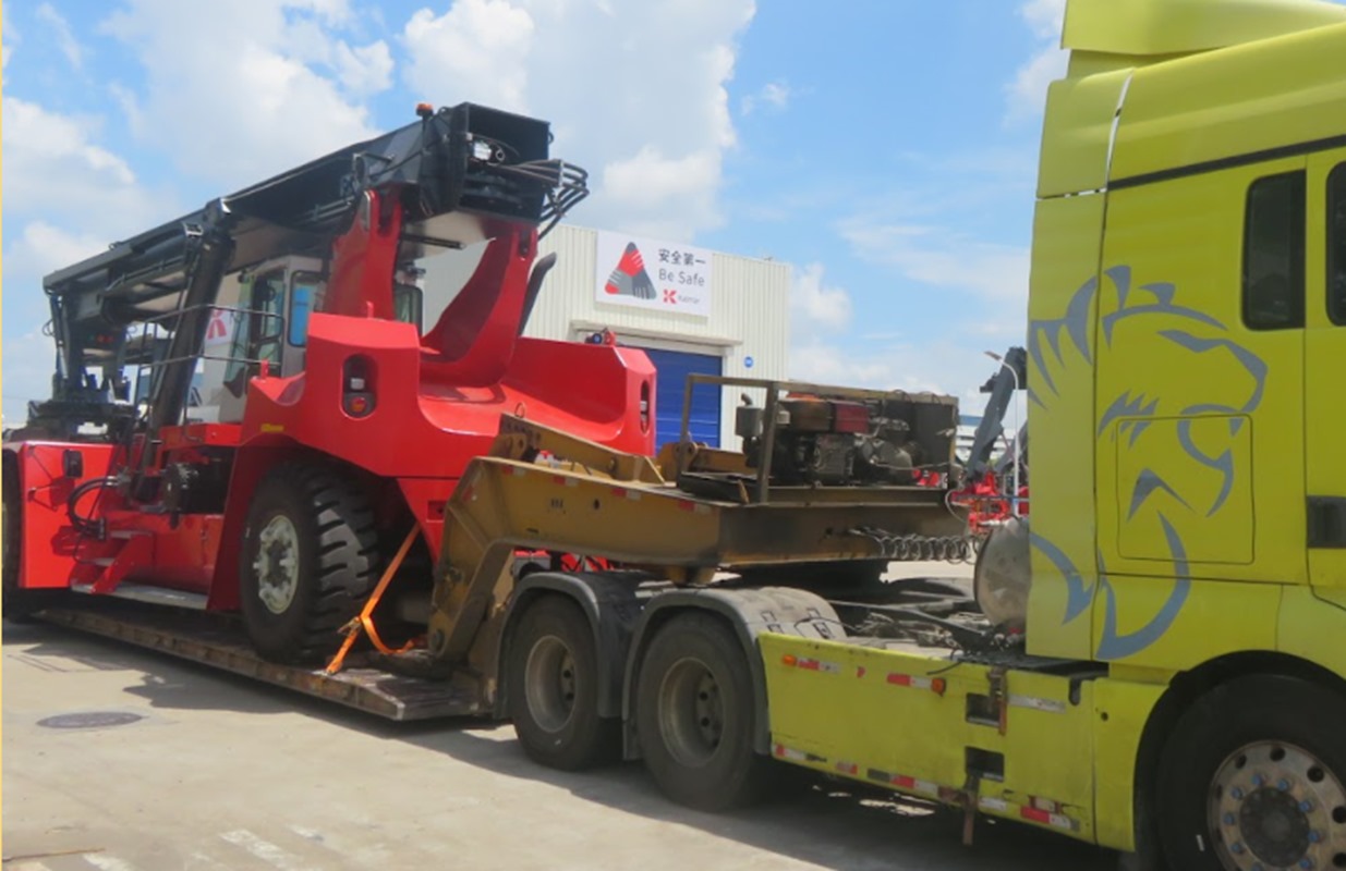 Yellow truck transporting red reach stacker